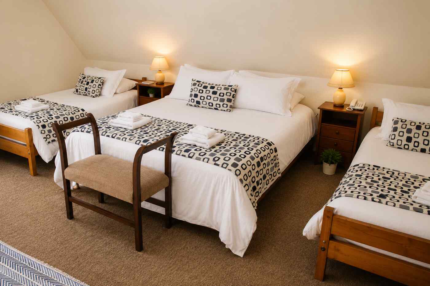 Classic quadruple room at Hotel Rondo Viña del Mar with one double and two single beds, warm bedside lamps and crisp white linens under a sloped attic ceiling